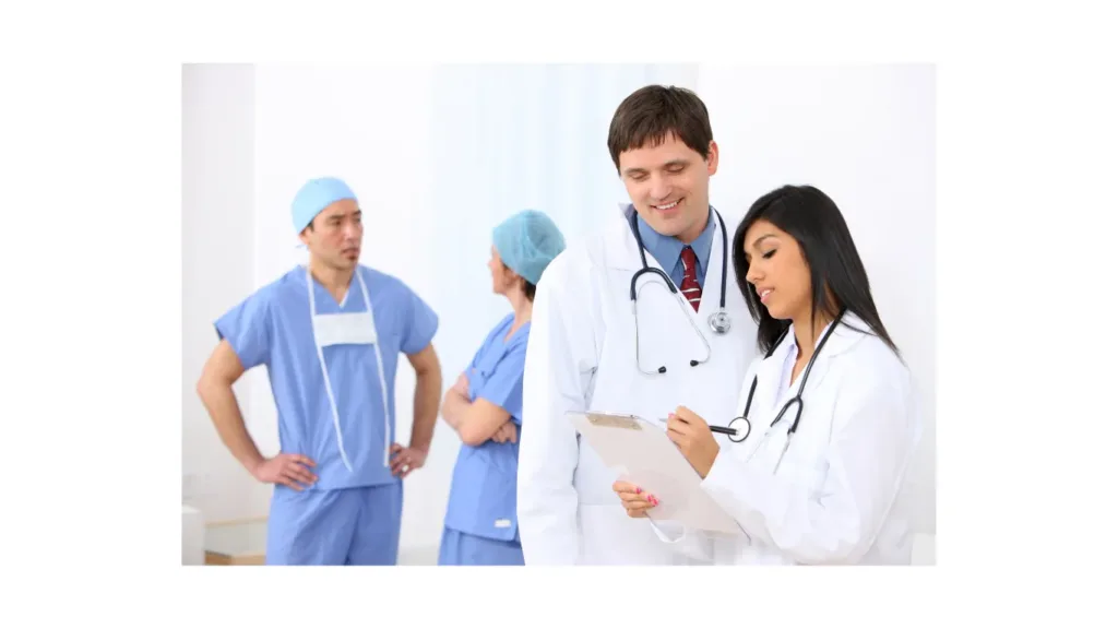 Two doctors reviewing a patient chart with nurses in the background